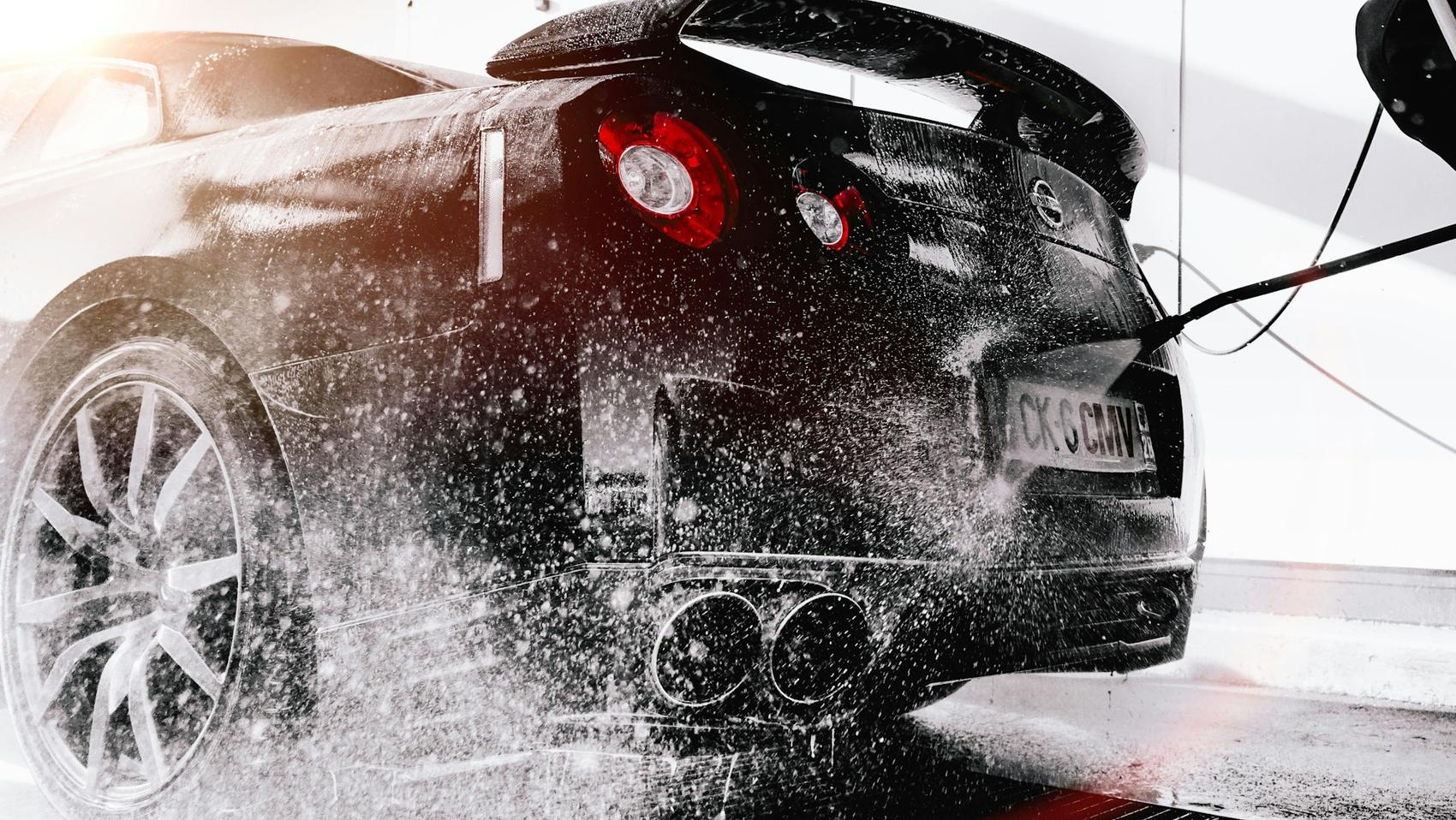 Mobile detailer rinsing a glossy black sports car