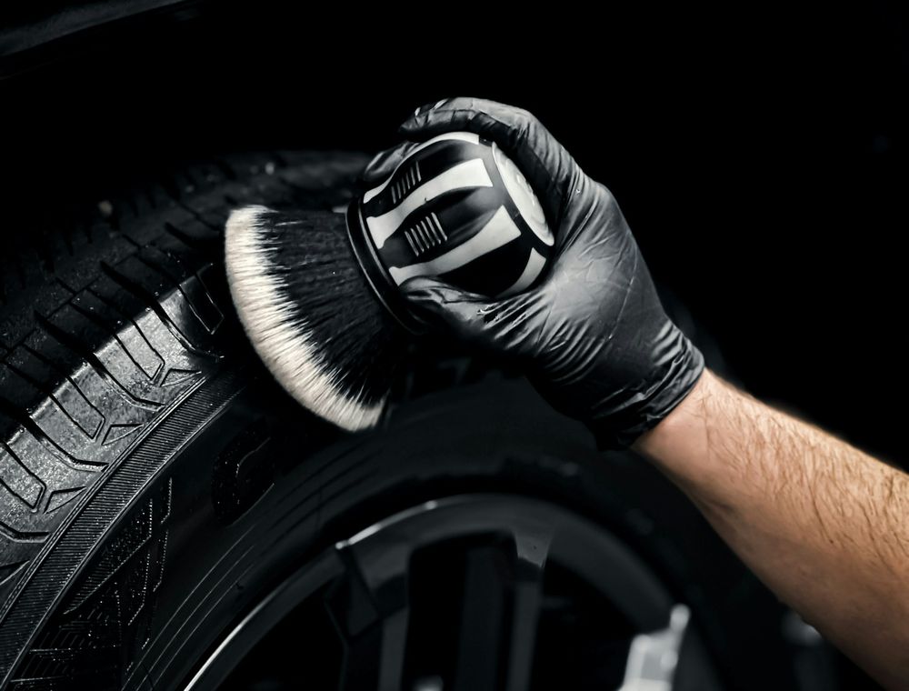 Gloved detailer brushing a clean alloy wheel